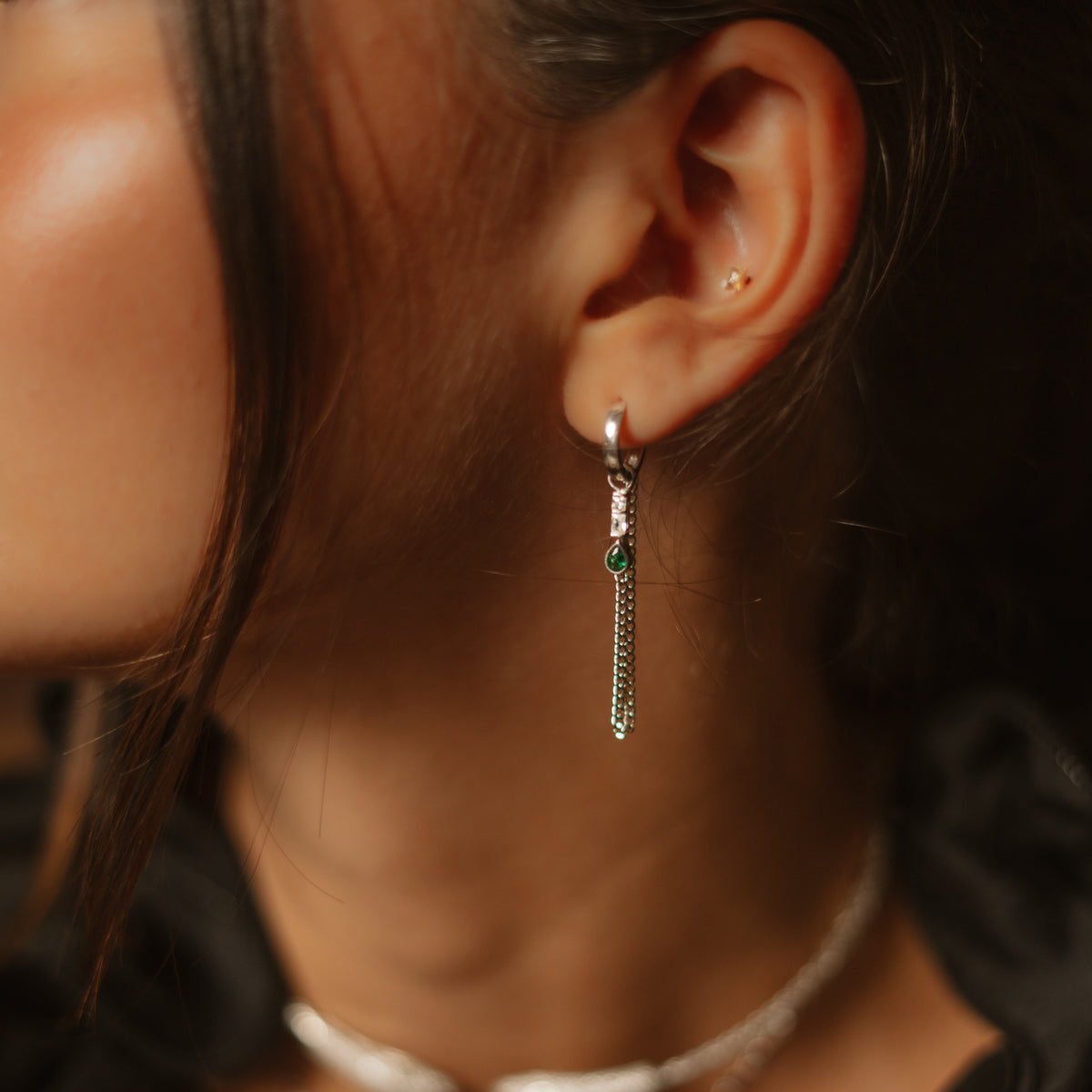 Side view of the sterling silver huggie earring with the double curb chain draping below the emerald