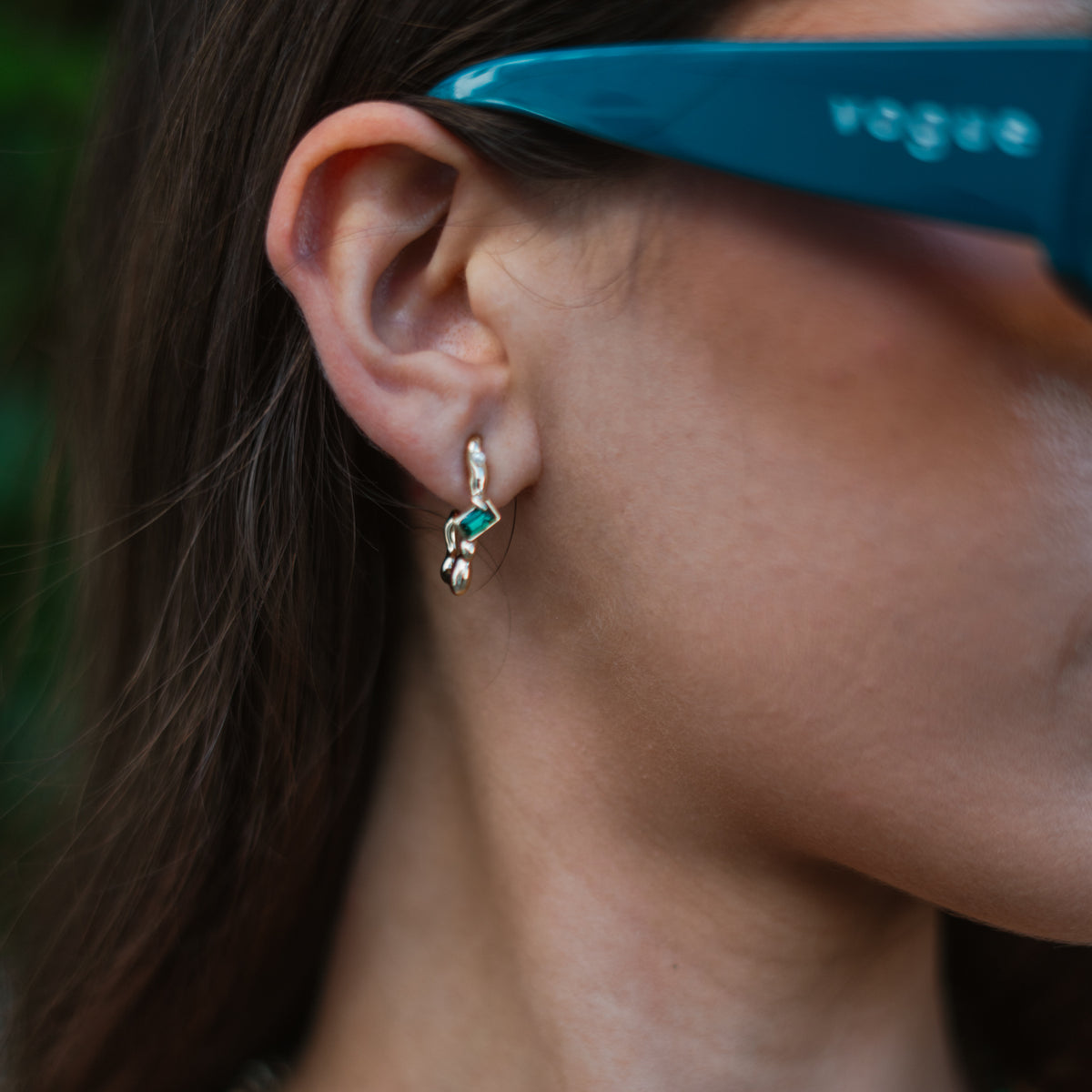 Close view of the Emerald Flow earring on the ear, the emerald cut green stone set in organic gold