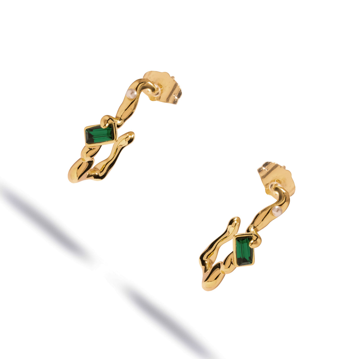 Angled studio view of the Emerald Flow pearl gold earrings, the molten gold hoops casting soft shadows