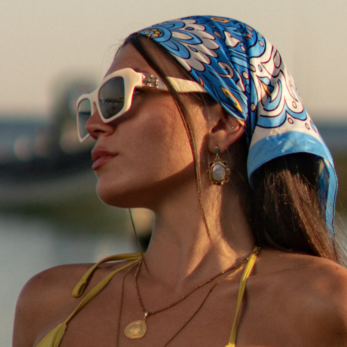 Profile view of a model wearing a baroque pearl multicolor gemstone gold drop earring below a blue silk headscarf
