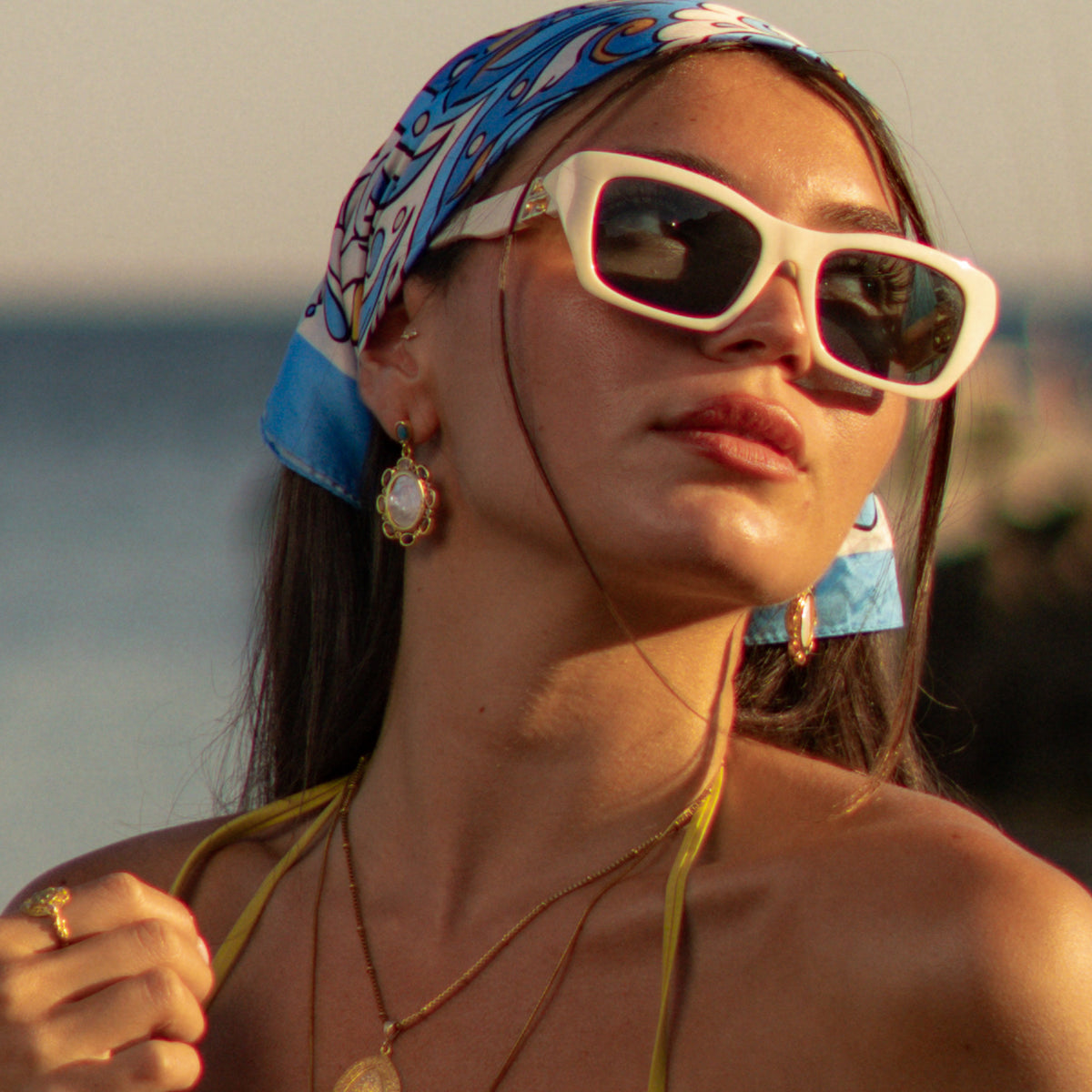 Model in white sunglasses wearing the baroque pearl gold drop earrings with a gold coin pendant necklace