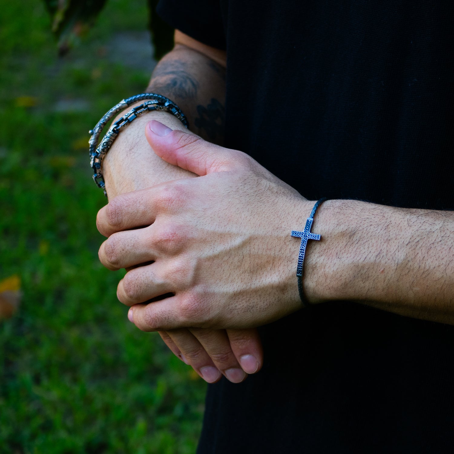 Sterling silver bracelet with woven band, bold cross centerpiece adorned with black diamonds, rhodium finish, masculine handcrafted design.