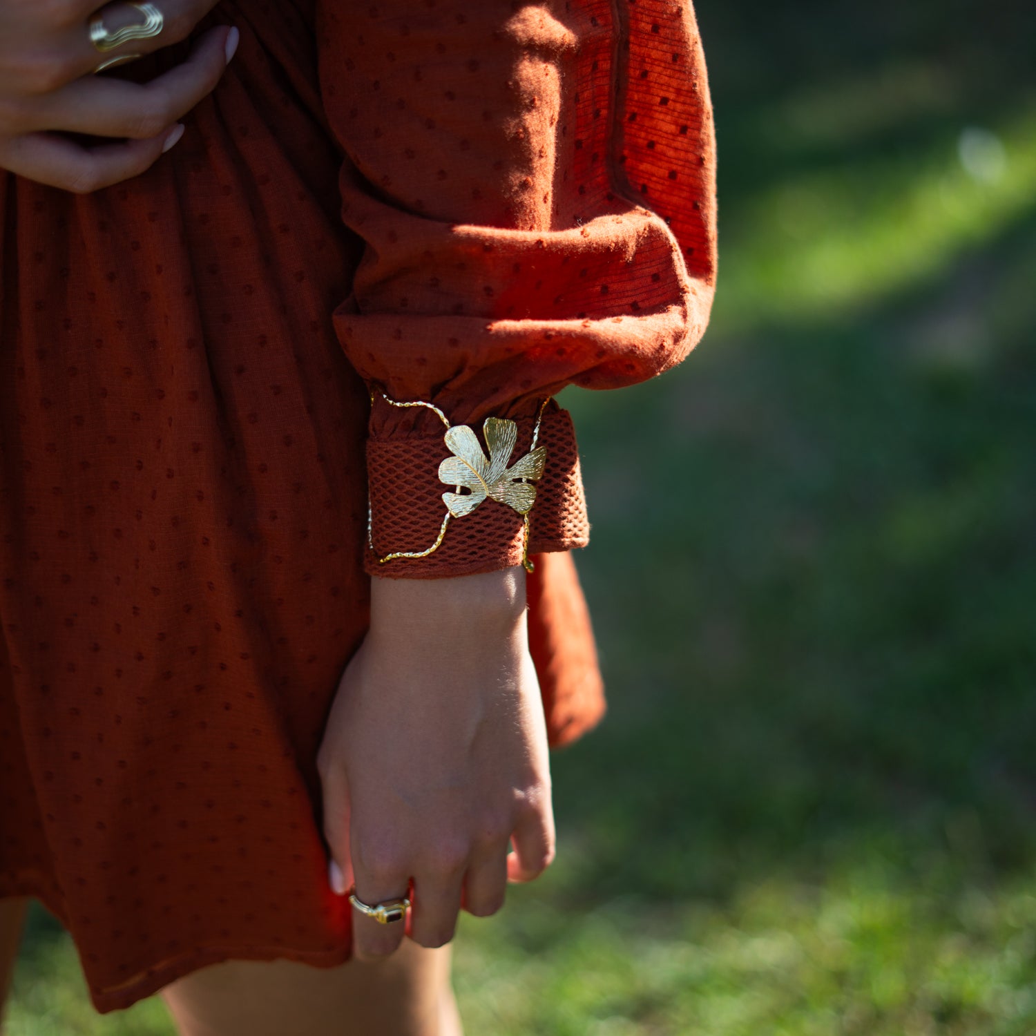 Person wearing a rust-colored dress with floral cuffs in a natural setting