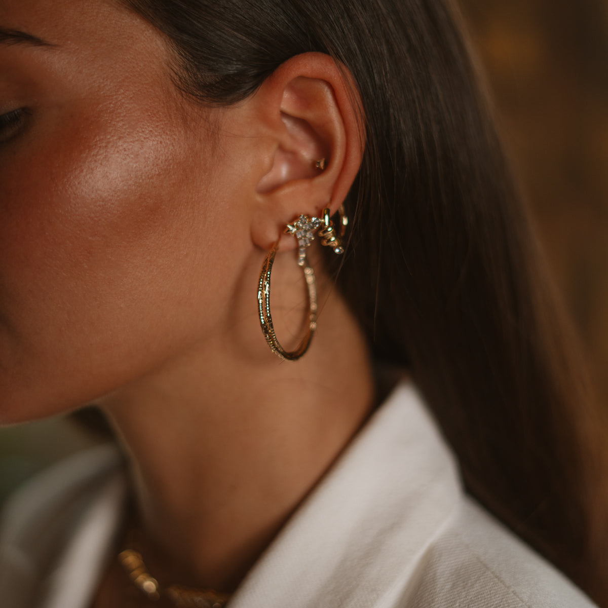 Close view of a model's ear wearing the gold twist hoop earring stacked with a smaller stone set hoop and ear cuffs
