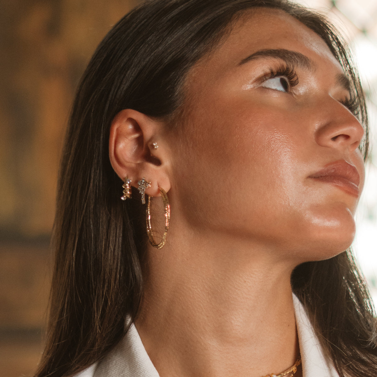 Side profile close up of a model's ear wearing the gold twist hoop earring with small crystal studs above it