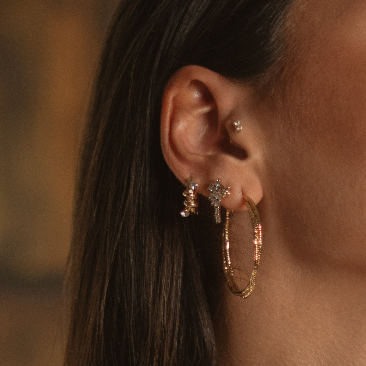 Macro close up of the gold twist hoop earring on the ear, showing the two ridged strands crossing over one another