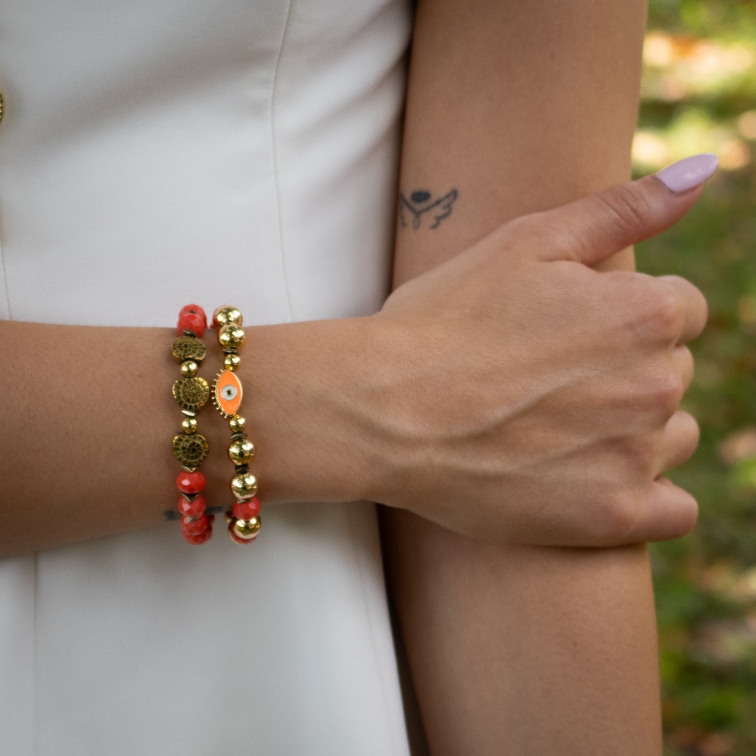 Handmade bracelet duo featuring orange enamel evil eye charm and gold shell symbols

