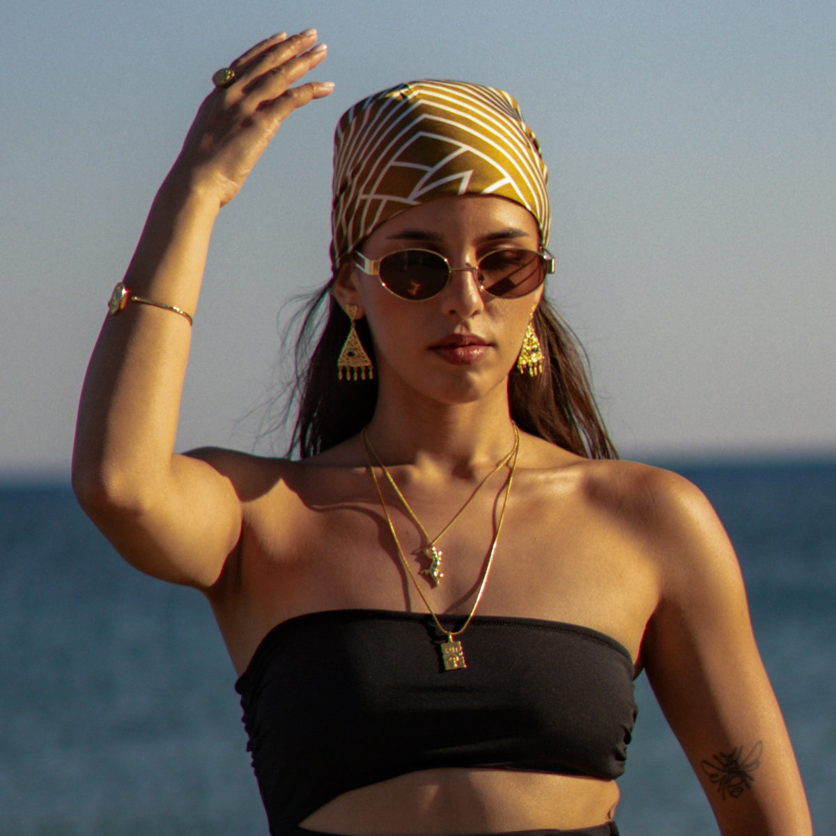 Model in sunglasses and a gold headscarf wearing the Exit pendant necklace layered with a gecko pendant