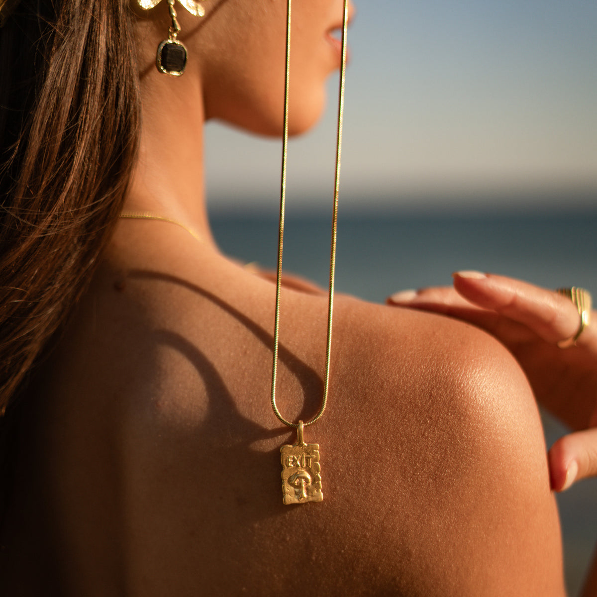 Exit engraved gold pendant on a long snake chain, worn over the shoulder by the sea