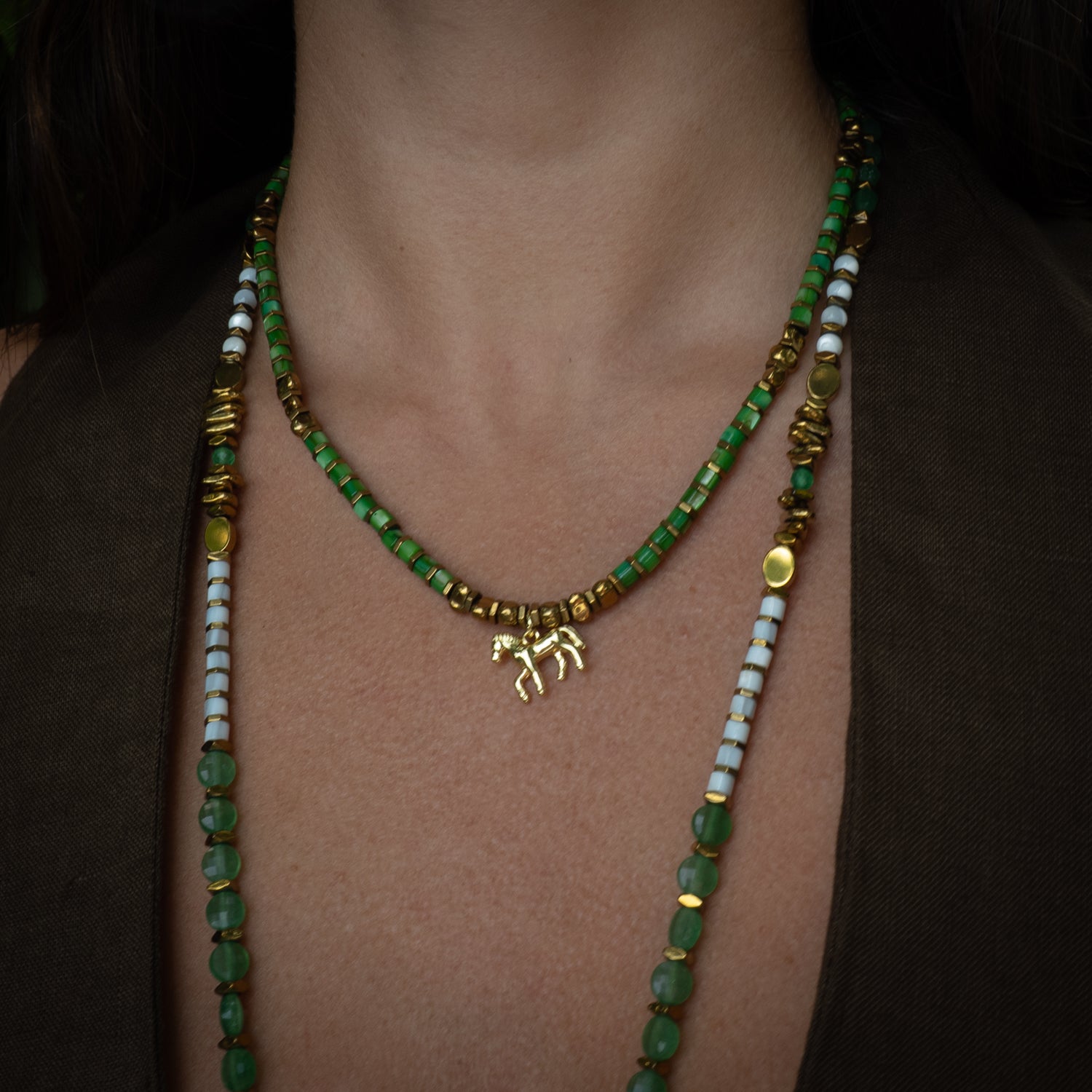 Model wearing green pearl beaded choker with horse charm at collarbone, layering jewelry styling
