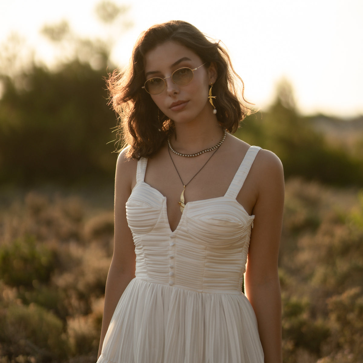 Model in a white dress in the countryside wearing the Free Spirit Sparrow Gold Pendant Two Tone Necklace
