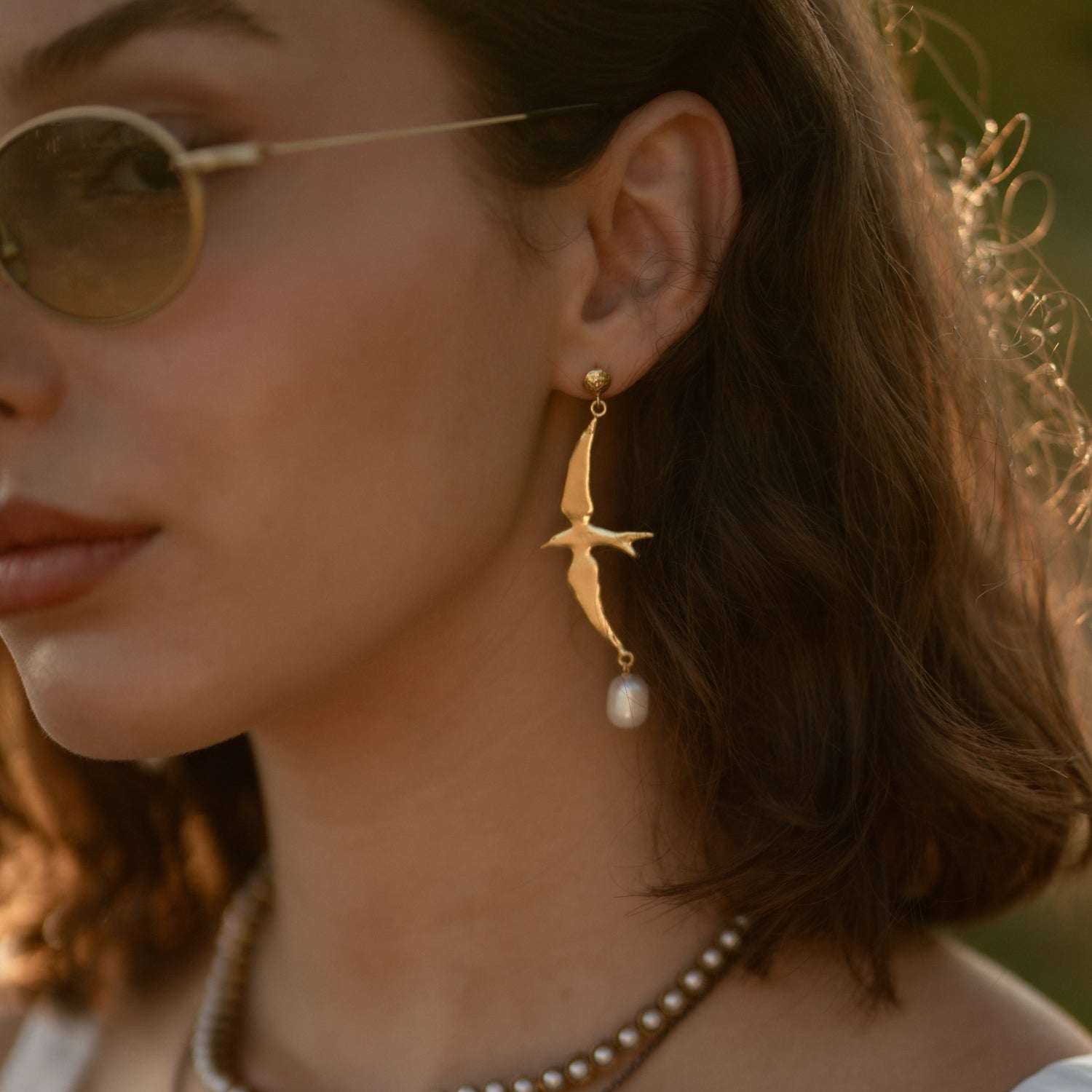 Free Spirit Sparrow Pearl Gold Drop Earring worn on the ear, gold sparrow in flight above a freshwater pearl drop