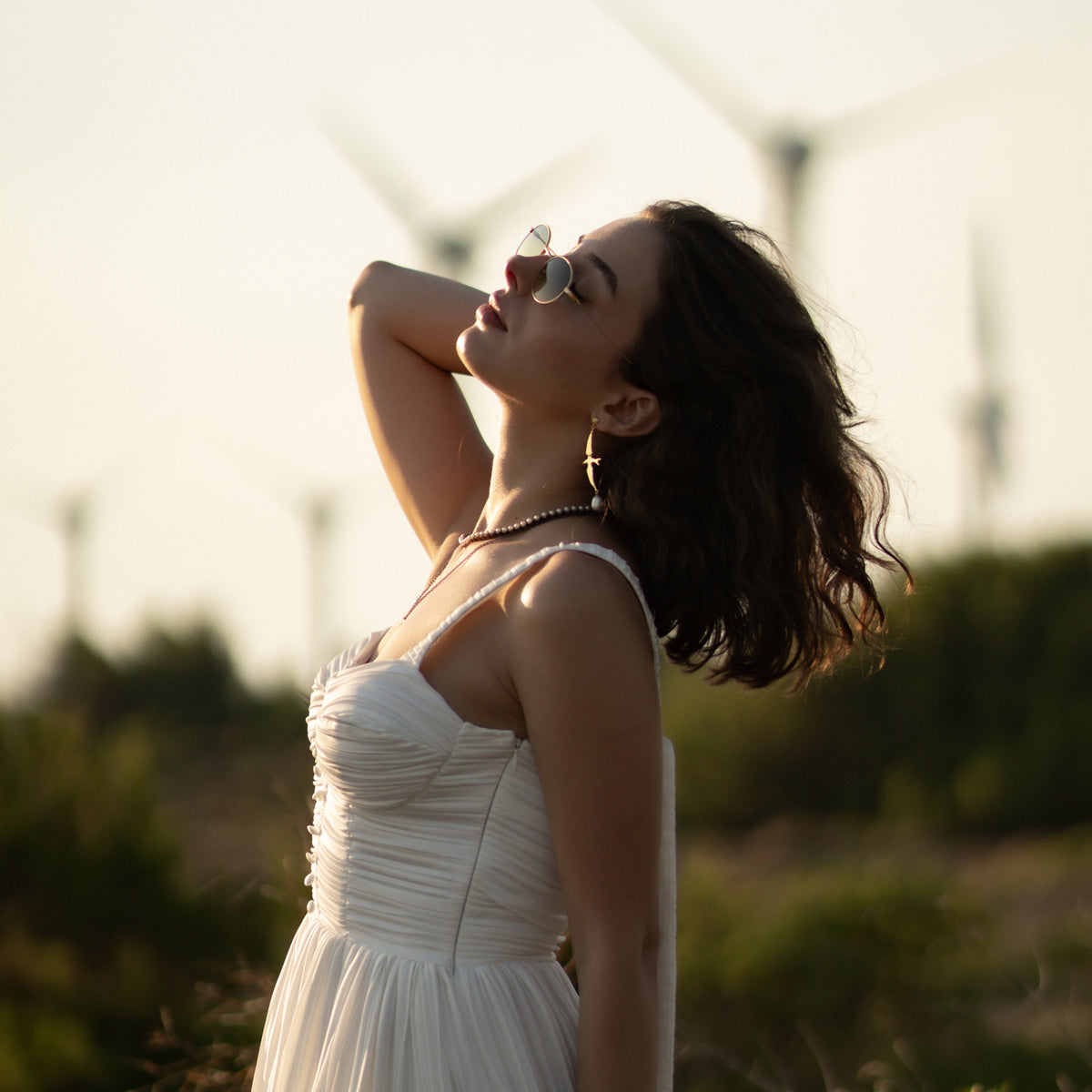 Woman in a white dress outdoors wearing the Free Spirit Sparrow Pearl Gold Drop Earrings