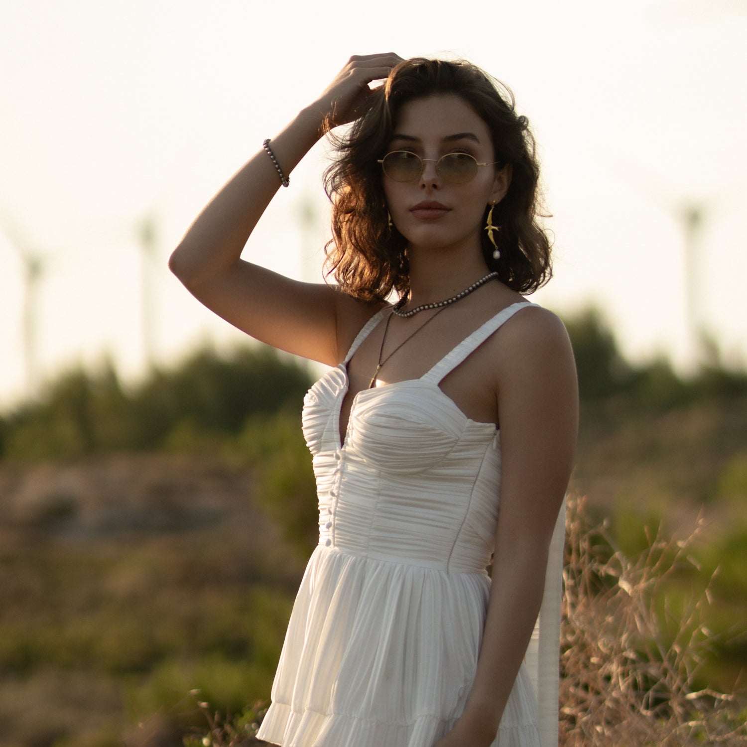 Model in sunglasses and a white dress wearing the Free Spirit Sparrow Pearl Gold Drop Earrings in the evening light