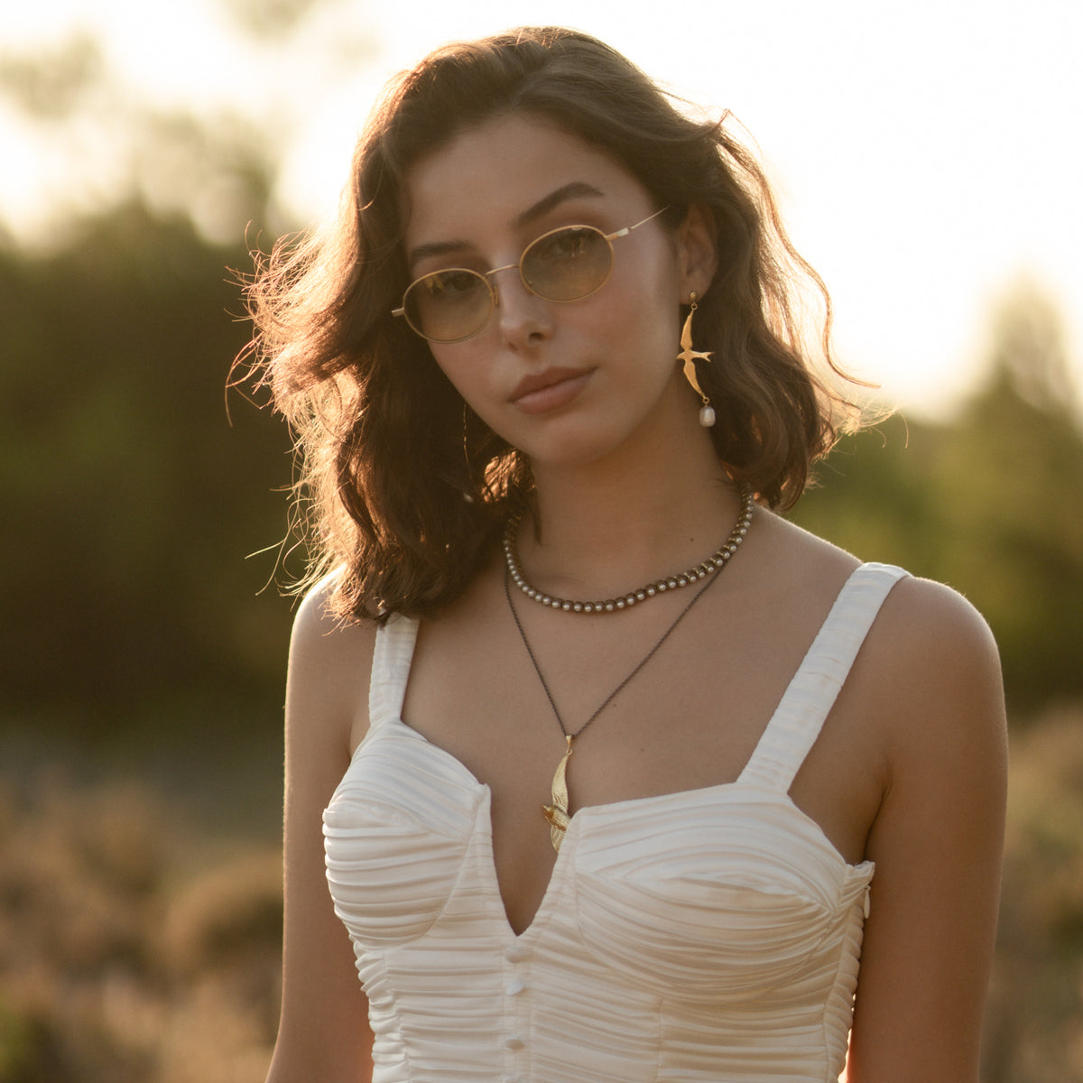 Free Spirit Sparrow Pearl Gold Drop Earrings worn with a white dress and layered beaded necklaces