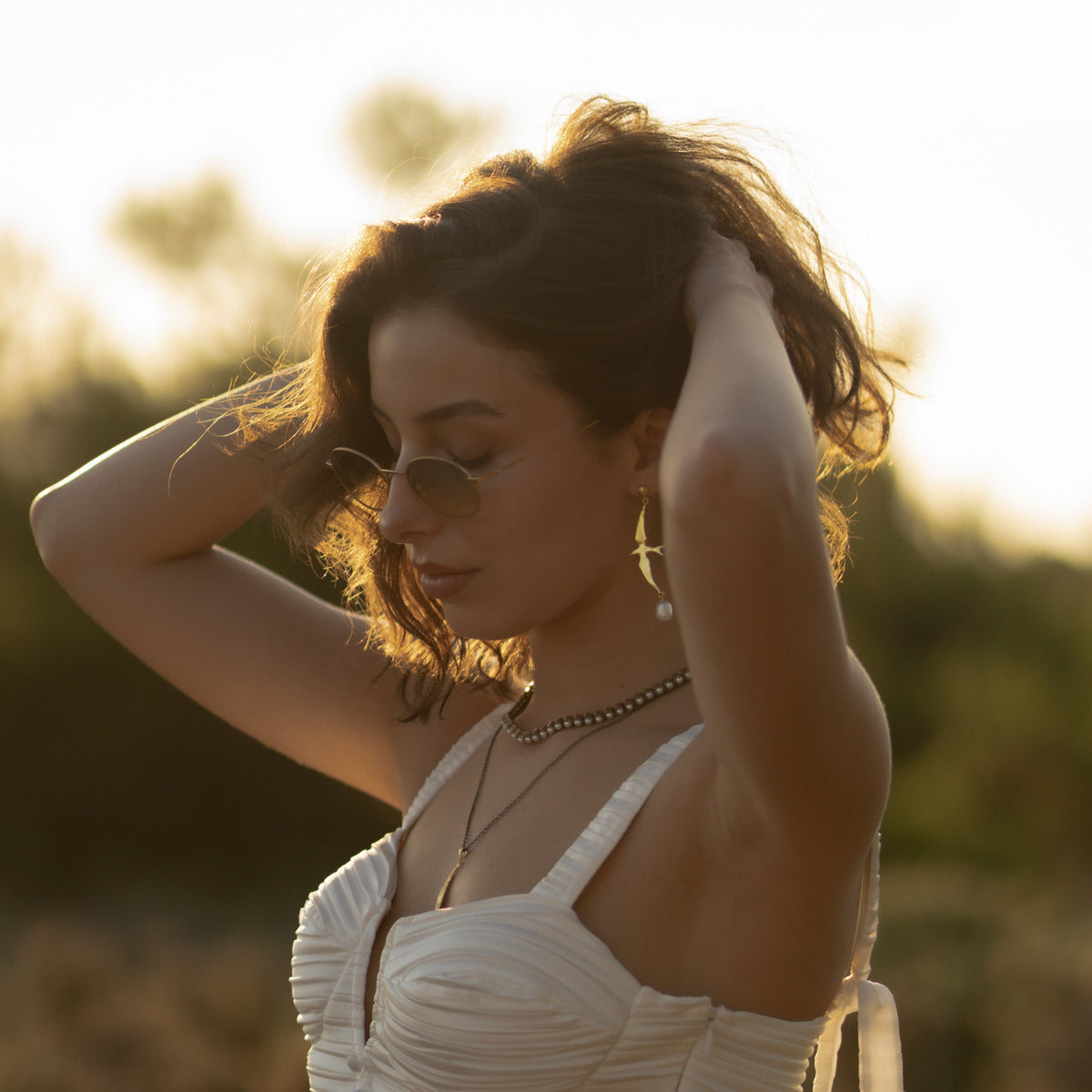 Model in a white dress at golden hour wearing the Free Spirit Sparrow Pearl Gold Drop Earrings