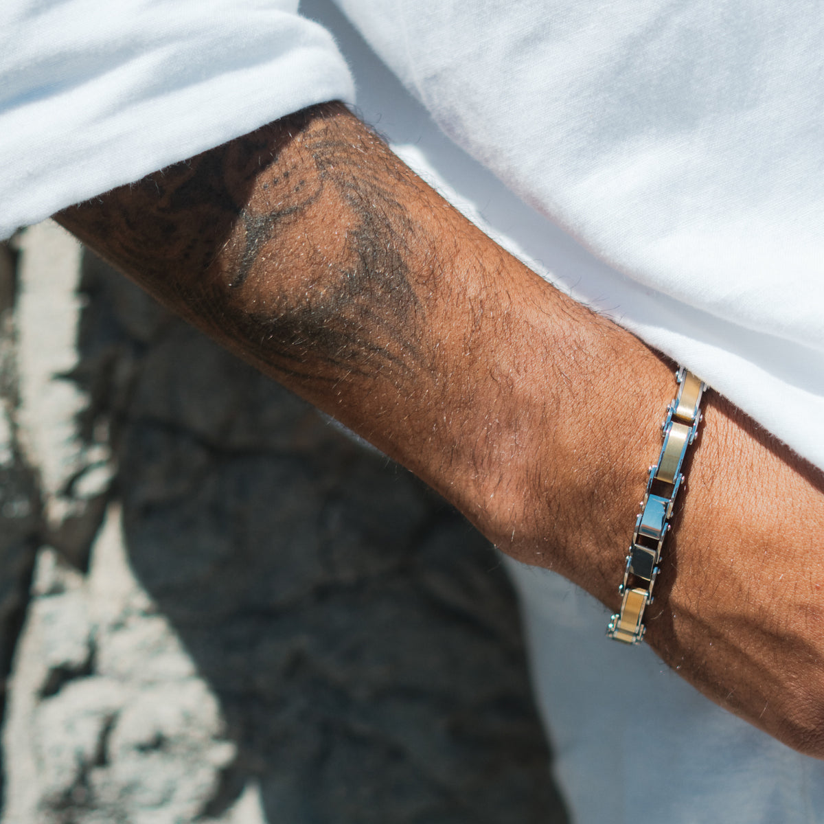 Two-tone stainless steel men's link bracelet on a sunlit wrist below a rolled white sleeve