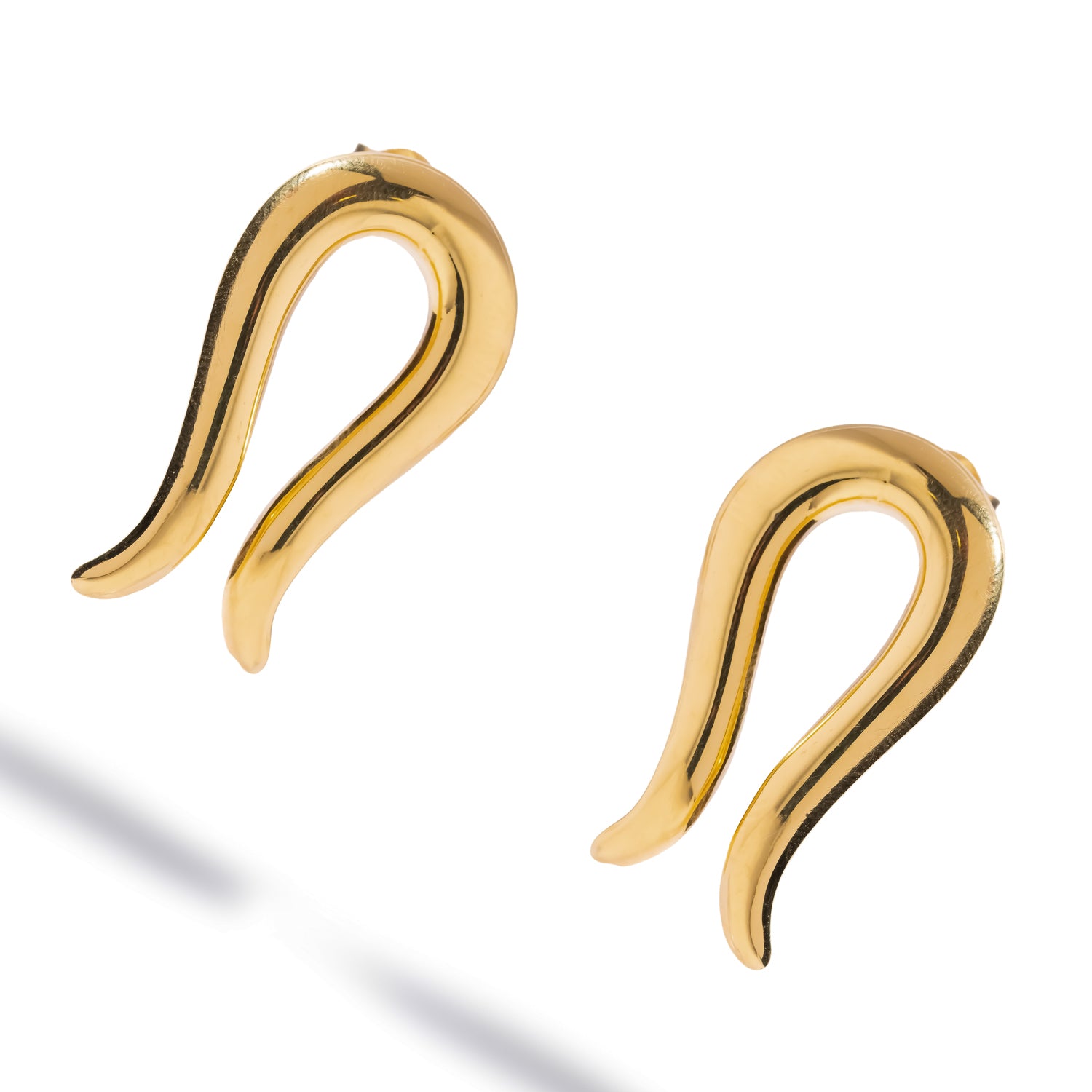 Golden Horseshoe Statement Stud Earrings laid flat at an angle, mirror-polished gold catching a diagonal streak of light