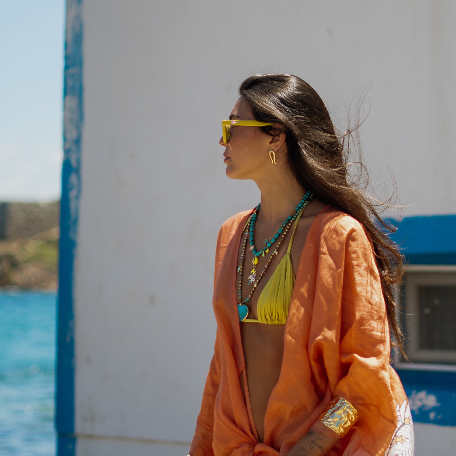 Model wearing the Golden Horseshoe stud earrings in a coastal lifestyle setting with turquoise jewelry and an orange cover-up