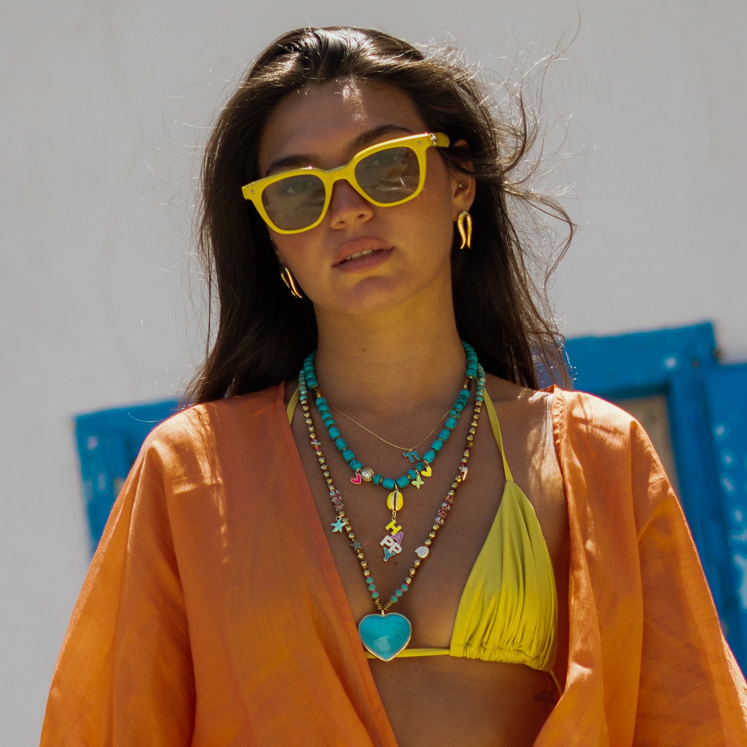 Model wearing the Golden Horseshoe stud earrings styled with yellow sunglasses and layered turquoise necklaces
