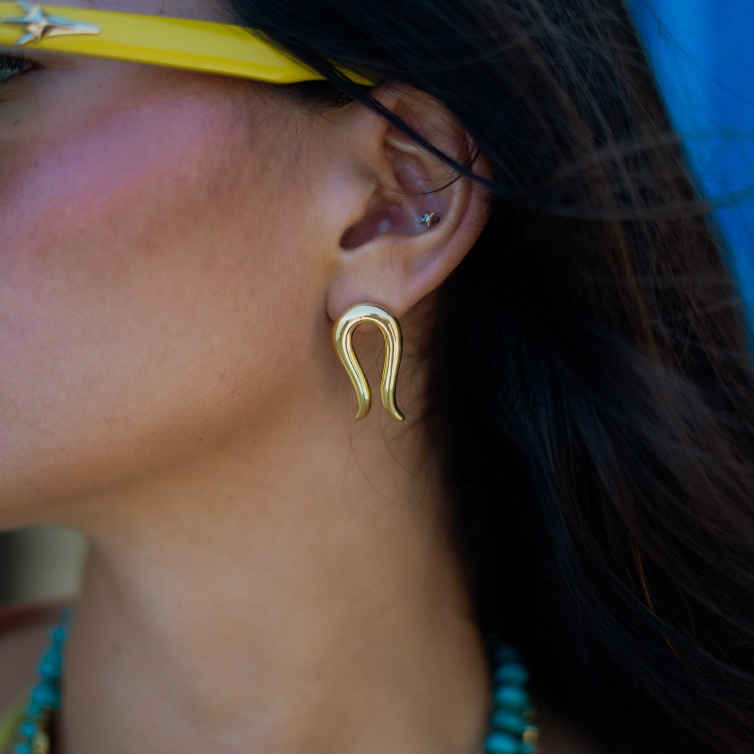 Close-up of the Golden Horseshoe stud earring worn on the ear, highlighting the open curve and tapered tip