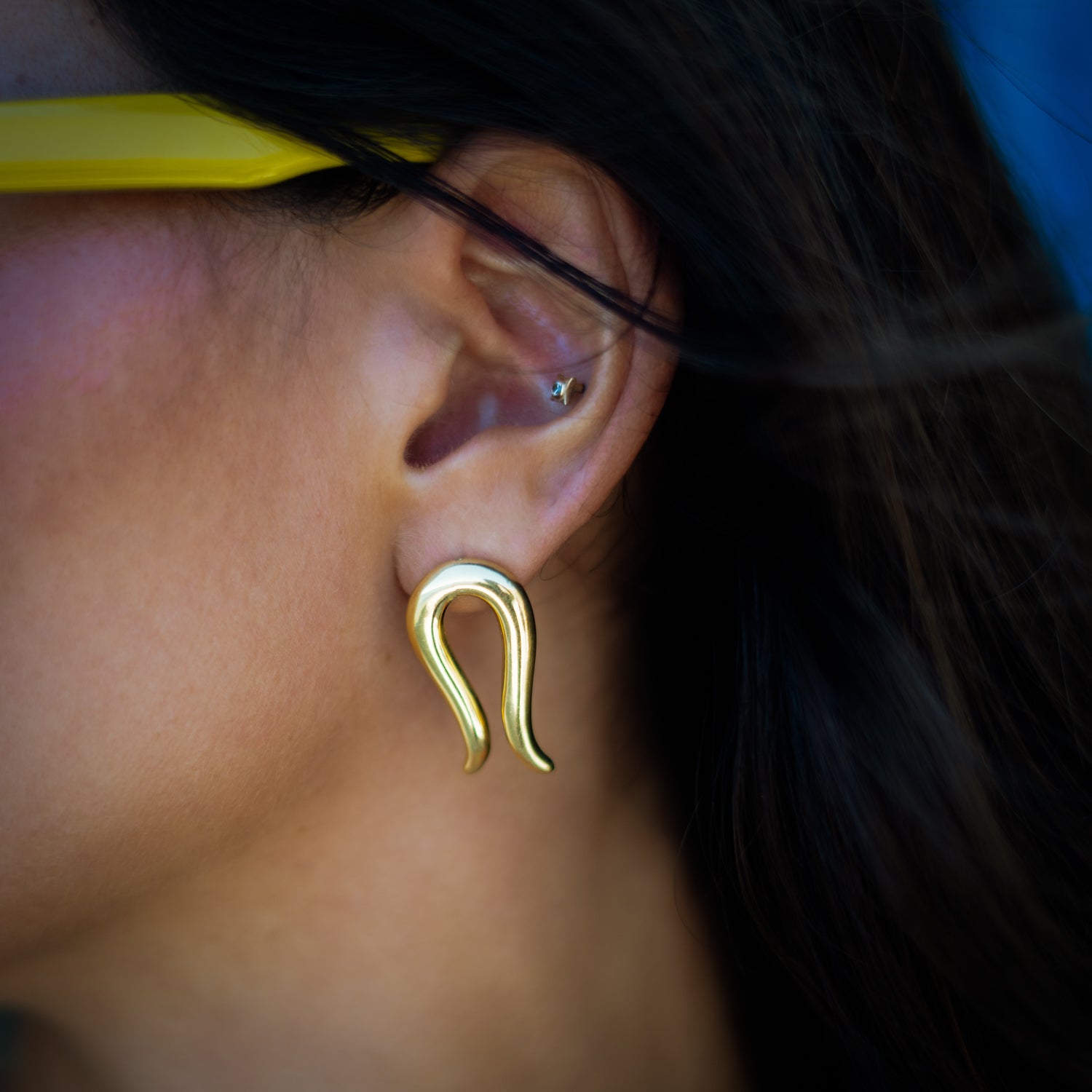Macro close-up of the Golden Horseshoe stud earring worn on the ear, showing the tapered gold curve in sharp detail