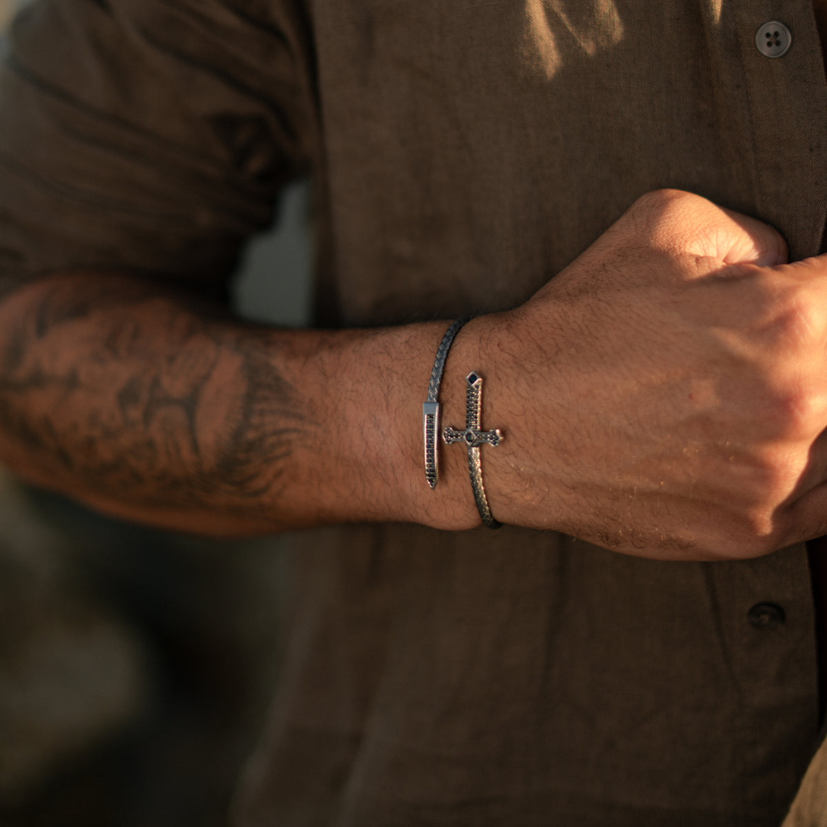 Oxidized silver wrap bracelet with a black stone Gothic cross and dagger point on a man's wrist in warm light