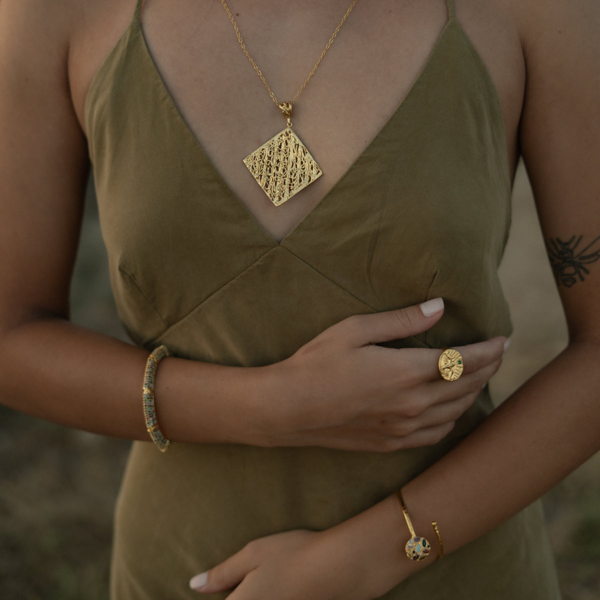 Model in an olive slip dress wearing the Guardian Emerald Eye gold ring with a gold square pendant and gold bracelets