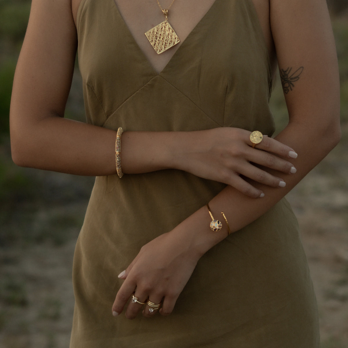 Model in an olive slip dress at dusk, the Guardian Emerald Eye gold ring on her hand with stacked gold bracelets