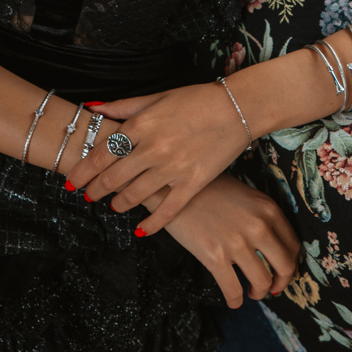 Hands crossed over a black lace dress, the Guardian Emerald Eye silver ring worn beside silver bangles and the Silver Rhythm link bracelet