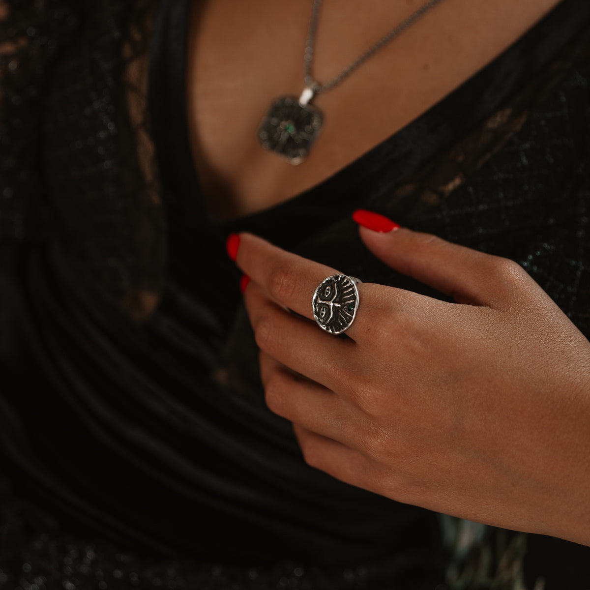 Guardian Emerald Eye sterling silver ring on the middle finger, hand resting on a black velvet neckline with a silver pendant