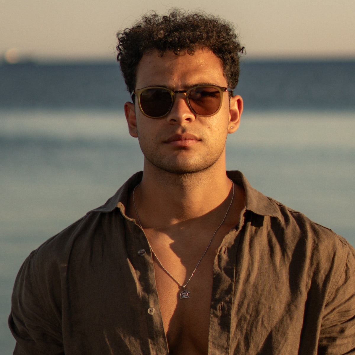 Man in an open linen shirt at the shore wearing the Guardian Falcon Emerald Eye Silver Men's Necklace