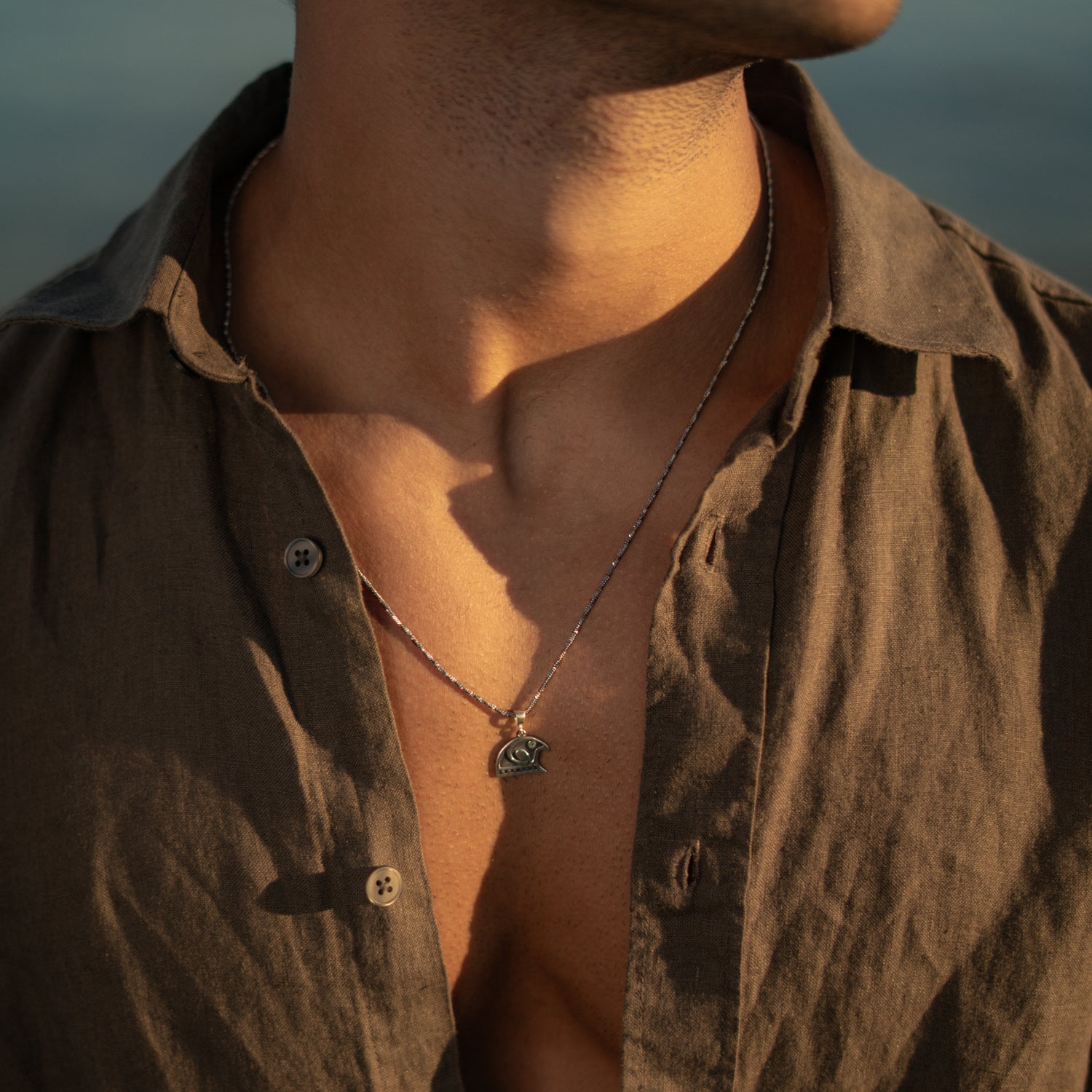 Detail of the Guardian Falcon Emerald Eye Silver Men's Necklace worn open collar, chain and pendant in warm evening light