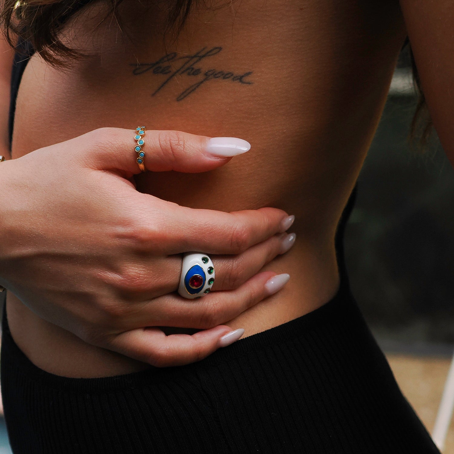 Striking white enamel ring featuring a guardian Evil Eye design with ruby and emerald stones on an 18K gold-plated band.
