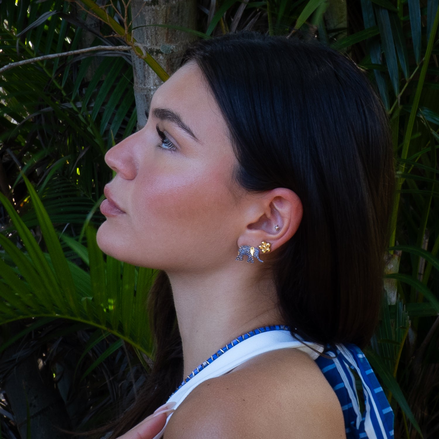 Woman wearing elephant earrings with a tropical background