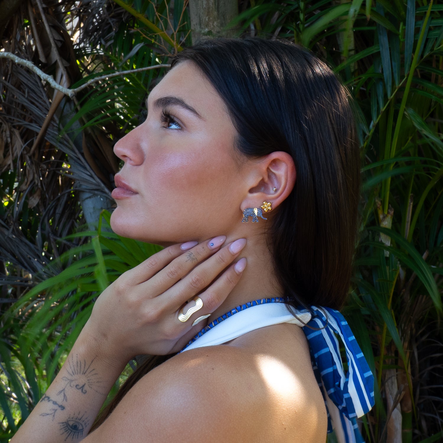 Woman with earrings and a tattoo, standing among green foliage