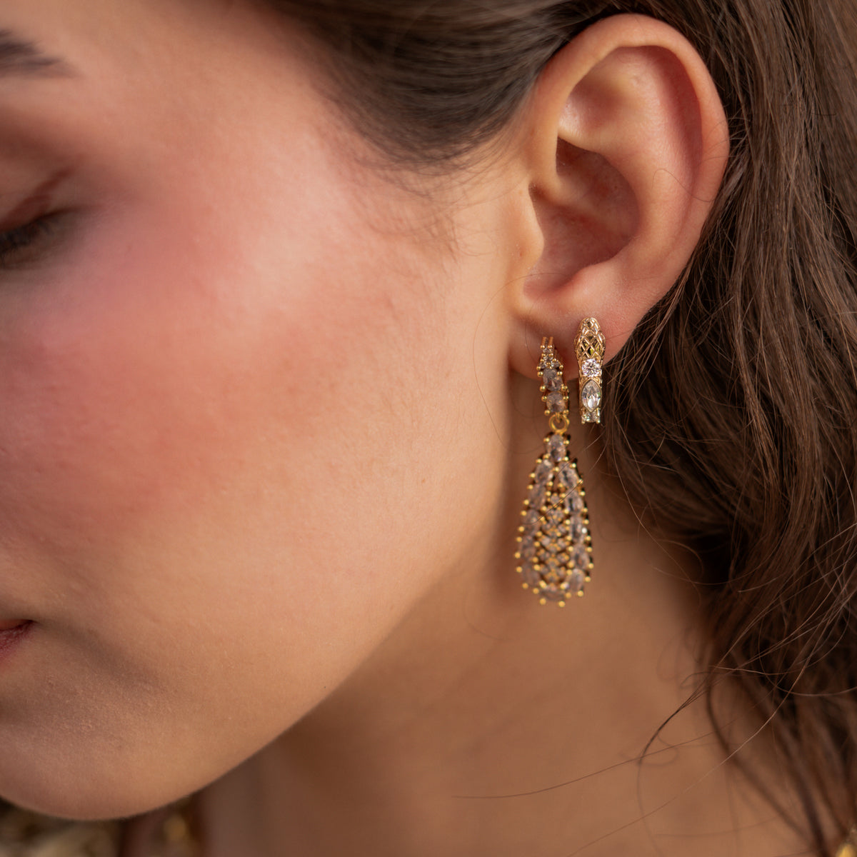 Guardian Serpent gold huggie hoop in a second piercing beside a crystal teardrop drop earring, showing the scaled head and zircon stones on the spine