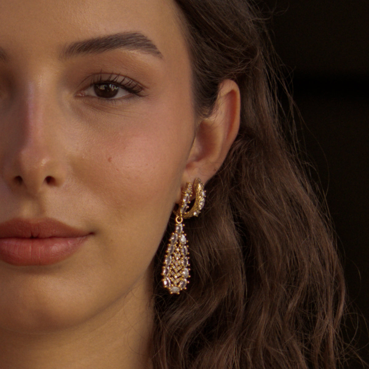 Close portrait of a model wearing the Guardian Serpent gold huggie hoop stacked with a crystal teardrop drop earring