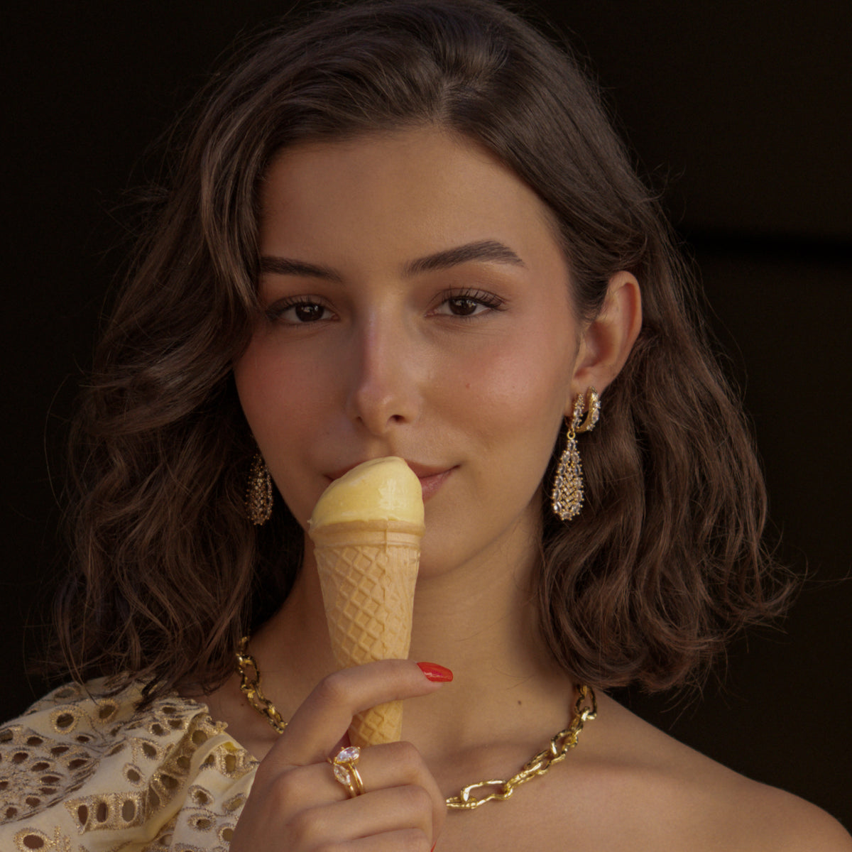 Model holding an ice cream cone, wearing crystal teardrop drop earrings stacked with the Guardian Serpent gold huggie hoop and a chunky gold link necklace