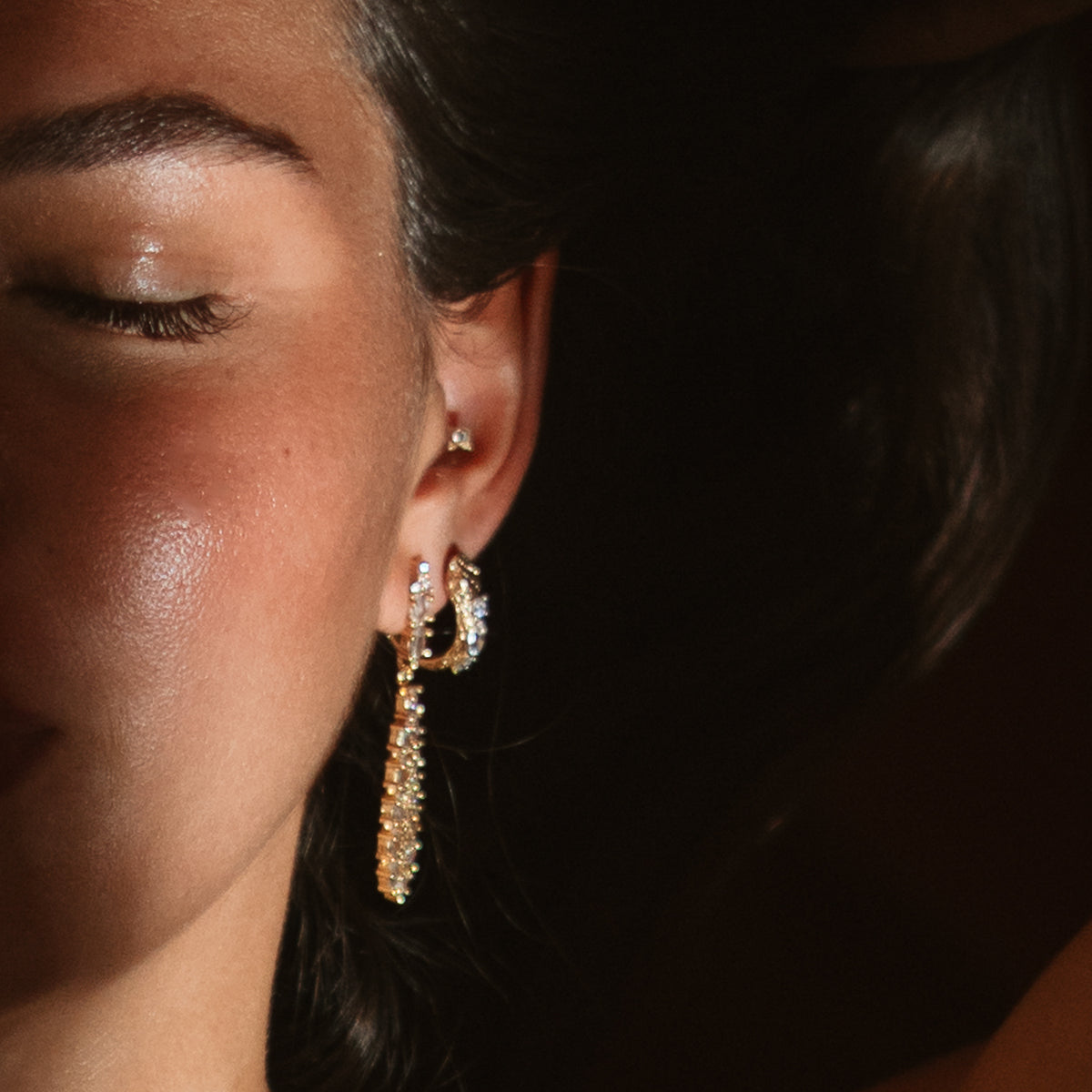 Close view of the Guardian Serpent gold huggie hoop worn beside a crystal fringe drop earring at the ear