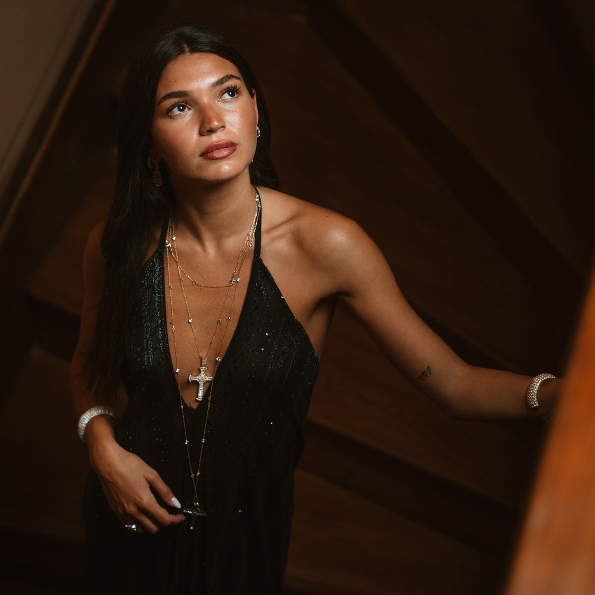Model on a staircase wearing a long gold cross necklace with a black dress