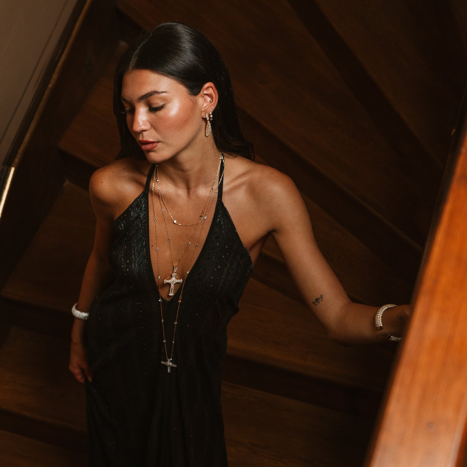 Long gold cross necklace worn low over a black dress, layered with a shorter chain