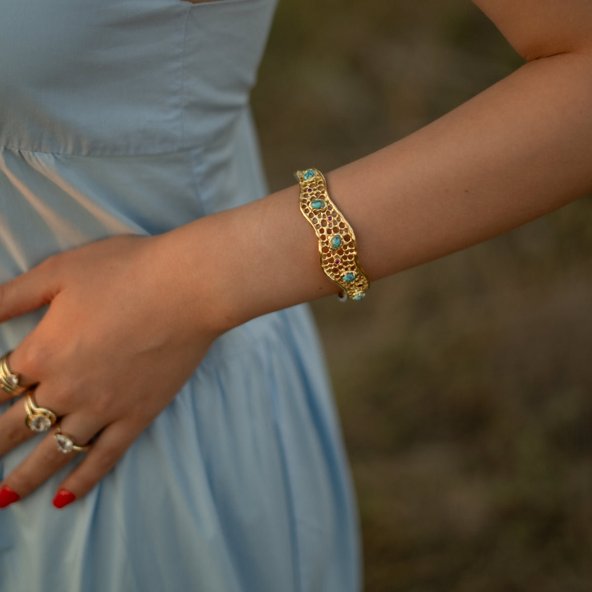 Honeycomb Lace Turquoise & Ruby Gold Cuff Bracelet worn on the wrist against a pale blue dress