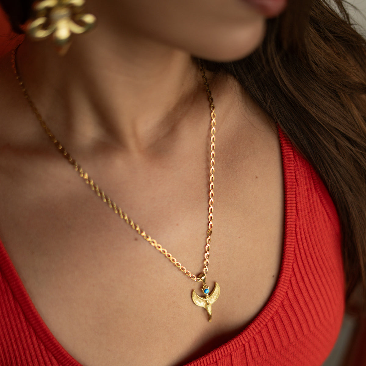 Woman in a red top wearing the Isis Goddess Opal Gold Pendant Necklace with ornate gold drop earrings