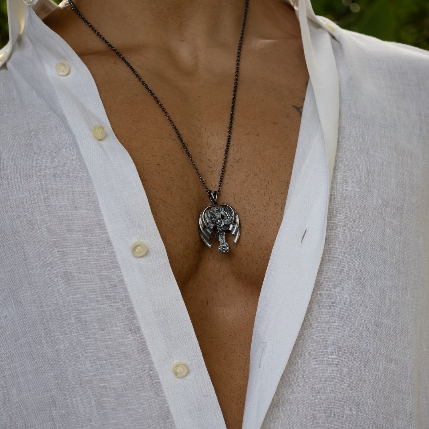 Sterling silver men’s necklace with detailed dragon entwined around cross pendant, rhodium-plated finish, textured scales and wings, bold design.