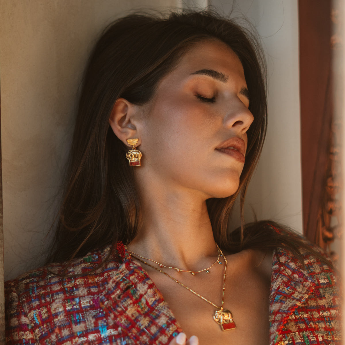 Model in a red tweed jacket wearing the Lucky Elephant Coral Mosaic Gold Drop Earrings with the matching elephant pendant necklace