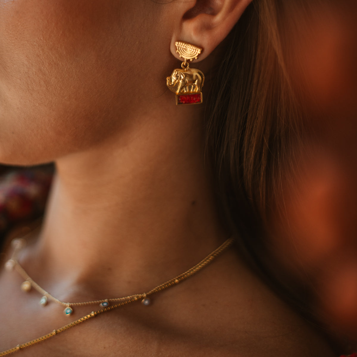 Close view of the Lucky Elephant Coral Mosaic Gold Drop Earring on the ear, the coral bar catching the light
