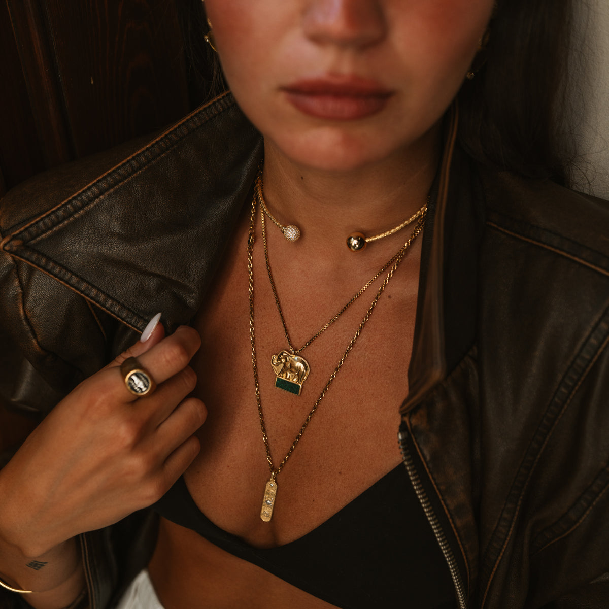 Close view of the emerald green mosaic elephant pendant layered with a gold torque choker and a long bar pendant