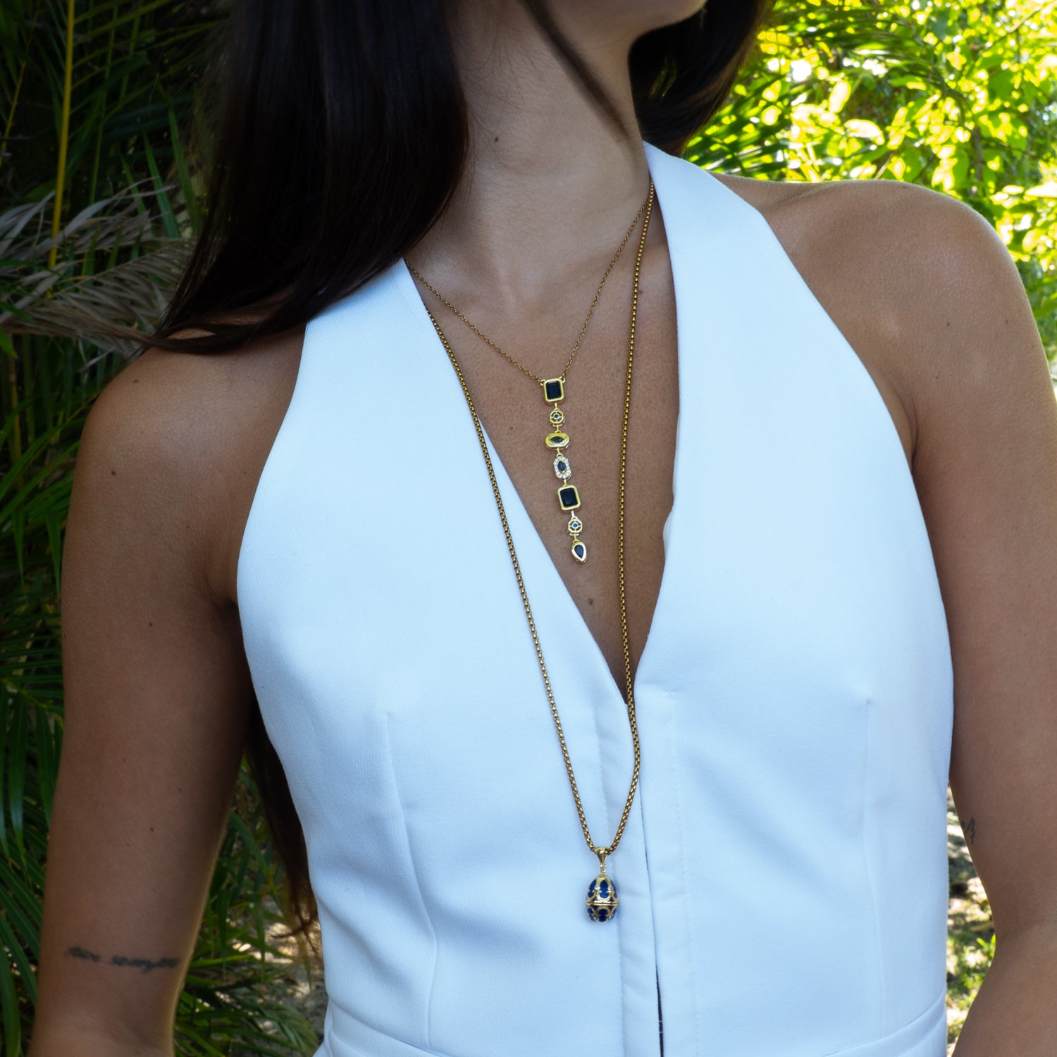 Woman wearing a white dress with a gold necklace against a green outdoor background