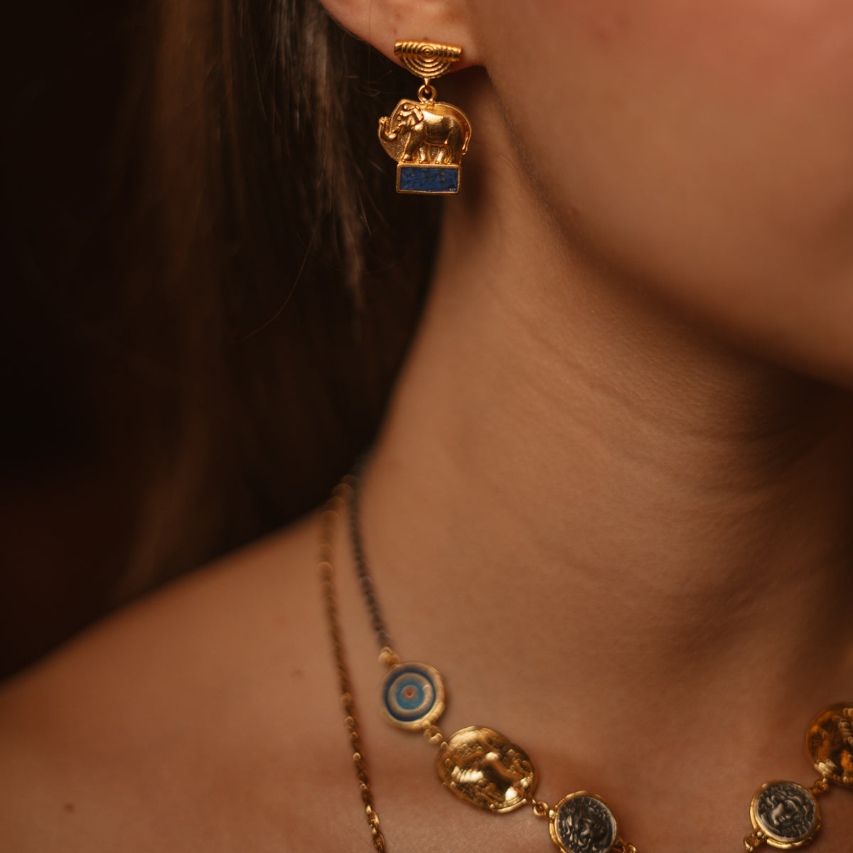 Close view of the Lucky Elephant Lapis Lazuli Gold Drop Earring on the ear with an Ebru Jewelry evil eye necklace below